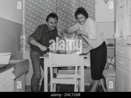 Noël en Allemagne 1962.Le père et la mère préparent le rôti traditionnel de festival, une dinde, dans la cuisine. Banque D'Images