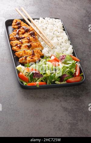 Le katsu de poulet est un plat traditionnel japonais servi avec de la salade de riz et de légumes dans l'assiette sur la table.Verticale Banque D'Images