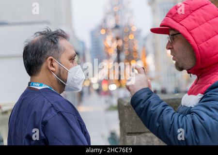 Londres Royaume-Uni 25December 2021.Le personnel de NSH explique à anti-vaxer dans le sweat à capuche rouge au sujet de la vaccination.Le personnel du NHS et les bénévoles de la communauté passent leur jour de Noël à l'hôtel de ville de Redbridge, offrant le vaccin contre le coronavirus, jingle jab pour toutes les personnes éligibles comme le meilleur cadeau de Noël de son genre, en maintenant tout le monde en sécurité car les cas d'Omicron sont trouvés doubler tous les deux jours.Credit: Xiu Bao/Alamy Live News Banque D'Images