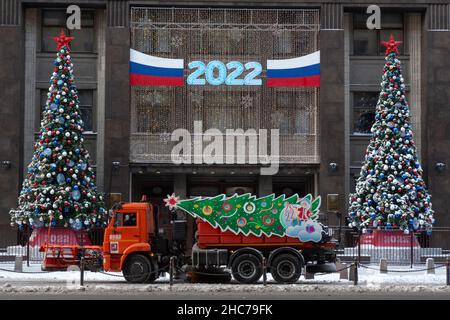 Moscou, Russie.25th décembre 2021 à la Saint-Sylvestre, un chasse-neige décoré de services municipaux de la ville descend dans la rue sur le fond d'une entrée avant décorée du nouvel an à la Douma d'Etat de la Fédération de Russie dans le centre de Moscou, en Russie Banque D'Images