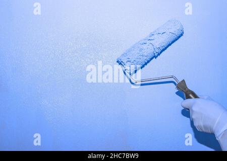 Travaux de peinture.Une femme peint le mur avec un rouleau avec de la peinture lilas, copier l'espace sur la gauche.La couleur de la tendance de l'année. Banque D'Images