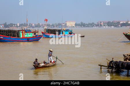 Petit bateau à perche avec 2 personnes devant les bateaux de pêche bleus à Day Hai, près de Hoi an. Banque D'Images