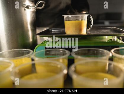 un chef dans un restaurant pèse un récipient de soupe, de la nourriture en plastique sur une balance, le processus de préparer une charité ou un déjeuner de bureau dans la cuisine Banque D'Images