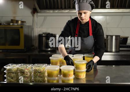 Livraison de la nourriture au restaurant. Le chef féminin prépare la nourriture dans un restaurant et la prépare dans des plats jetables. Banque D'Images