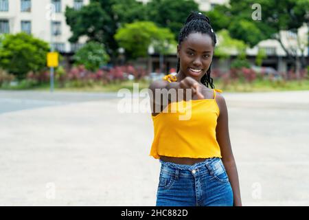 Pointant de jeunes femmes africaines américaines adultes avec des tresses à l'extérieur en été dans la ville Banque D'Images