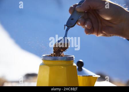 Homme randonneur qui fait du café de près depuis le pot de moka jaune en plein air dans les montagnes d'hiver enneigées.Vieux style café pot vintage camping extérieur Banque D'Images