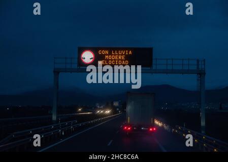 Panneau lumineux d'une autoroute lors d'une nuit de pluie avec la légende « sous la pluie, vitesse modérée » Banque D'Images