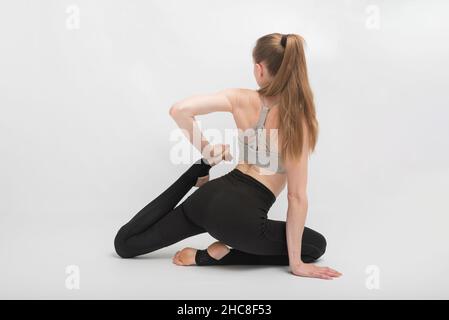 Jeune femme mince fait un exercice de flexibilité sur fond blanc.La fille est engagée dans la gymnastique ou le yoga Banque D'Images