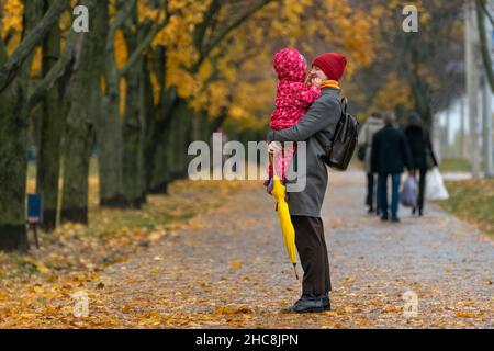 Mère tient le bébé dans ses bras contre le fond d'un parc d'automne.Marche avec les enfants. Banque D'Images