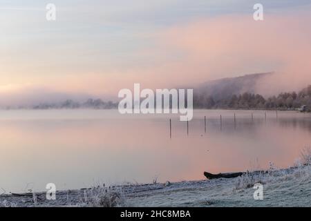 Magnifique lever de soleil en hiver avec des reflets dans le lac et du brouillard sur l'eau, créant un cadre de conte de fées avec des couleurs pastel lisses Banque D'Images