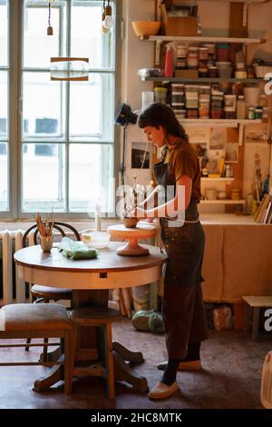 Une jeune femme potier travaille avec de l'argile sur la roue de poterie dans un espace créatif ou un studio professionnel Banque D'Images