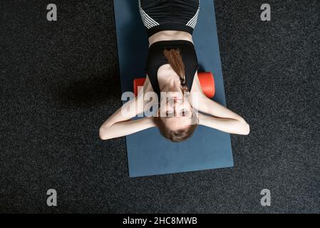 Une jeune fille sportive se trouve sur des rouleaux MFR.Femme fait un massage du dos avec un rouleau myofascial.Version myofasciale.Vue de dessus. Banque D'Images