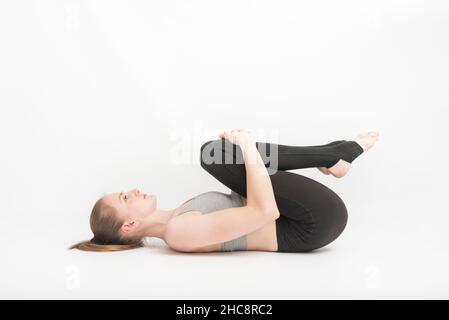 La jeune femme fait du yoga avec ses genoux à sa poitrine sur fond blanc.Technique d'exécution des asanas. Méditation Banque D'Images