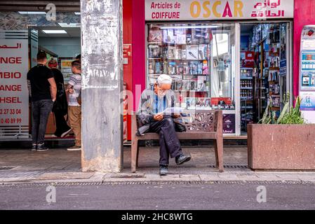 Homme de premier plan lisant des journaux assis sur le banc à côté de la route Banque D'Images