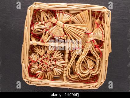 Un ensemble de jouets de Noël en paille en forme d'ange, coeur, flocons de neige et étoiles dans une boîte de paille sur une pierre d'ardoise, gros plan, vue de dessus. Banque D'Images