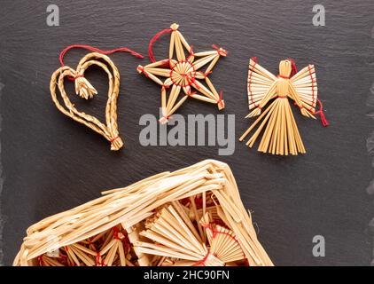 Trois jouets de Noël en paille sous forme de flocons de neige, un ange et une étoile sur une pierre de l'ardoise, gros plan, vue du dessus. Banque D'Images