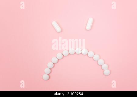 Préjudice pharmaceutique. Angry Smiley visage fait de pilules blanches, couché sur le Backgrond rose. Industrie pharmaceutique mondiale et médicaments Banque D'Images