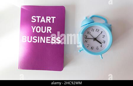 Commencez votre travail texte écrit sur un bloc-notes framboise et un fond blanc avec une horloge. Banque D'Images