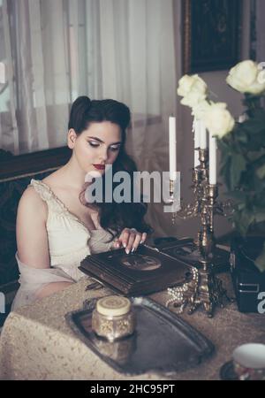 Une jeune femme regarde un album photo. Style vintage, intérieur rétro. Banque D'Images