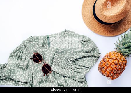 Style été décontracté.Vêtements et accessoires femme élégants.Robe, lunettes de soleil, chapeau et ananas sur fond blanc.Flat lay, vue de dessus. Banque D'Images