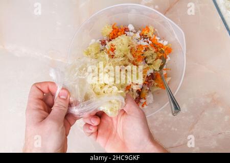 Un homme ajoute le chou congelé à la viande hachée pour les petits pains de chou paresseux sur la table. Banque D'Images