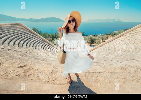 Élégante et charmante femme en robe blanche et chapeau explore les sites historiques et les ruines de l'amphithéâtre grec ou romain sur la côte de la station balnéaire de la Médite Banque D'Images