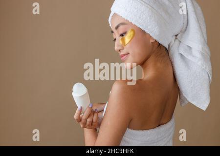 Jeune femme asiatique avec des taches sous les yeux tenant le déodorant Banque D'Images