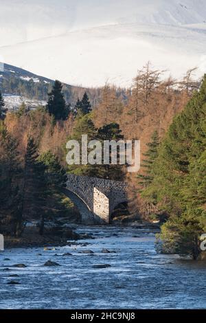 Le vieux pont de Dee à Invercauld sur le domaine Balmoral vu le long de la rivière et vu entouré par la forêt avec Snowy Hills au loin Banque D'Images