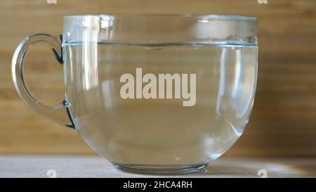 Verser de l'eau chaude dans une grande tasse transparente sur fond de bois flou.Vue latérale d'une tasse vide et le processus de poring de l'eau chaude pour les morni Banque D'Images