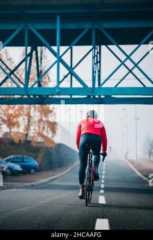 Vue arrière d'un jeune cycliste sympa en rouge, qui fait du vélo un jour sombre Banque D'Images