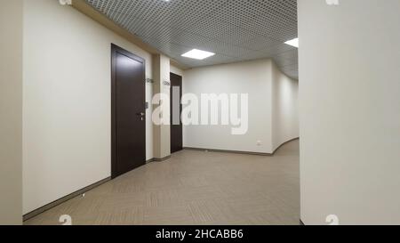 Couloir vide et rond avec murs beige clair et portes fermées marron foncé.Portes fermées le long d'un couloir éclairé dans l'immeuble de bureaux Banque D'Images