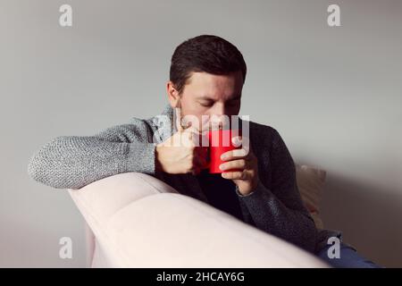 Un homme avec une tasse de café rouge dans la main portant un gilet.Le concept de l'automne.Vue avant. Banque D'Images