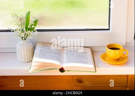 un livre ouvert, un bouquet de lys de la vallée et une tasse de café du matin sur le seuil de la fenêtre du cottage. le concept d'un séjour agréable Banque D'Images