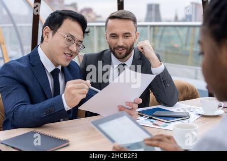 Jeune homme d'affaires asiatique en costume montrant le contrat à son partenaire et expliquant ses conditions avant de signer Banque D'Images
