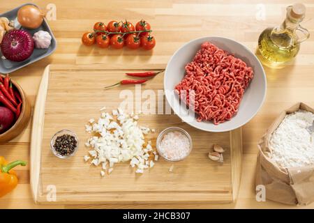 Plat de tomates fraîches, oignon cru haché, poivre, ail, huile d'olive,farine et viande hachée sur une table de cuisine en bois Banque D'Images