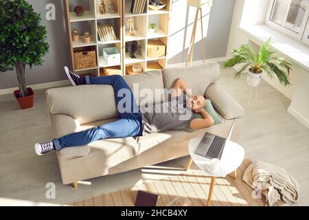 Homme prenant une pause de travail sur un ordinateur portable et se nappant sur un canapé confortable dans la salle de séjour Banque D'Images