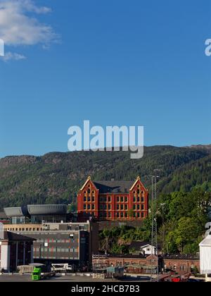 Ancien bâtiment norvégien traditionnel situé sur la colline surplombant le port de Bergen, entouré d'arbres et de nouveaux développements. Banque D'Images