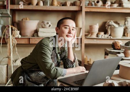 Portrait d'une jeune artisan regardant l'appareil photo tout en travaillant sur un ordinateur portable sur son lieu de travail en studio Banque D'Images