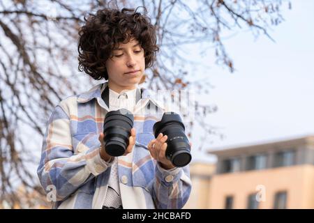 Jeune femme brunette avec des cheveux bouclés choisissant un objectif pour son appareil photo Banque D'Images