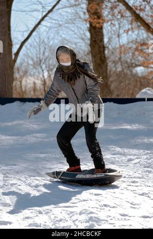 Une femme active dans ses 50s traîneaux sur une colline enneigée pendant un hiver froid.Dans un parc à Flushing, Queens, New York. Banque D'Images