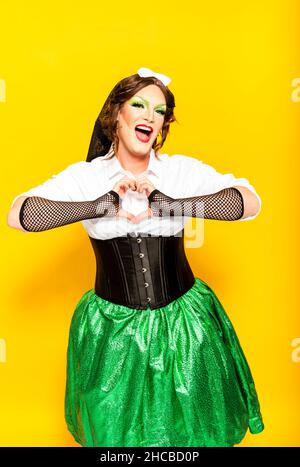 Hommes souriants dans le costume de la reine de drag tenant les fans colorés par fond jaune Banque D'Images