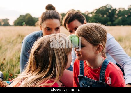Parents regardant des filles jouer avec des fruits dans le parc Banque D'Images