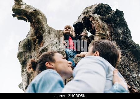 Fille souriante debout sur le tronc de l'arbre avec les parents dans le parc Banque D'Images