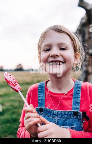 Fille souriante avec fente crantée tenant la lollipop dans le parc Banque D'Images