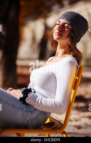 Adolescente portant un chapeau en tricot assis sur une chaise au parc Banque D'Images