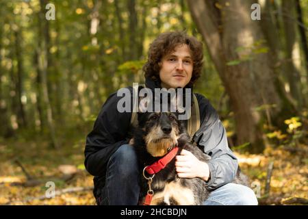 Homme souriant avec un chien assis dans la forêt Banque D'Images