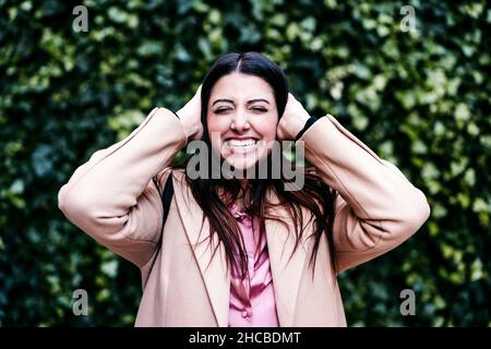 Femme d'affaires souriante couvrant les oreilles devant les plantes Banque D'Images