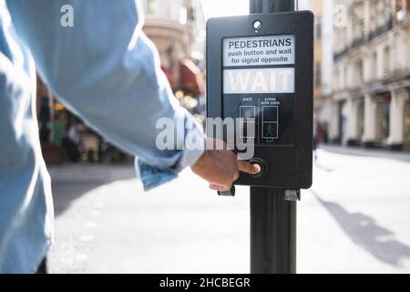 Homme appuyant sur le bouton du signal de circulation en ville Banque D'Images