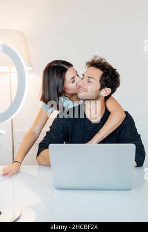 Une jeune femme embrasse un petit ami tout en travaillant à domicile Banque D'Images