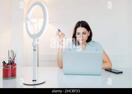 Jeune femme d'affaires avec un stylo travaillant sur un ordinateur portable dans le bureau à domicile Banque D'Images